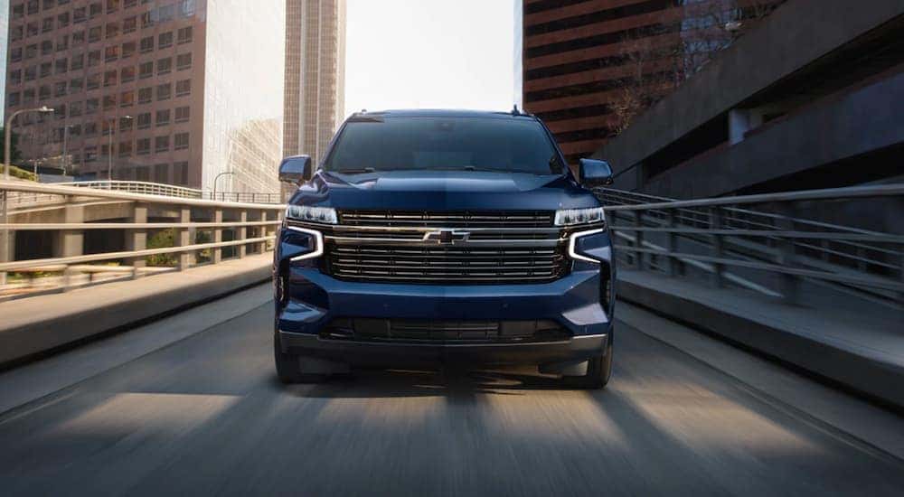 A blue 2024 Chevy Tahoe is shown from a front angle while driving over a bridge.
