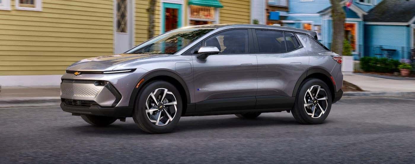 A silver 2024 Chevy Equinox EV is shown driving on a city street.