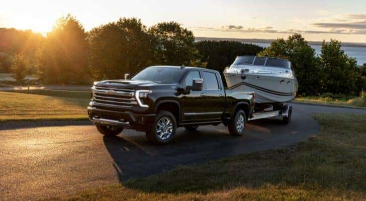 A black 2024 Chevy Silverado 2500HD High Country is shown towing a boat after visiting a Chevy dealer near Hyde Park.