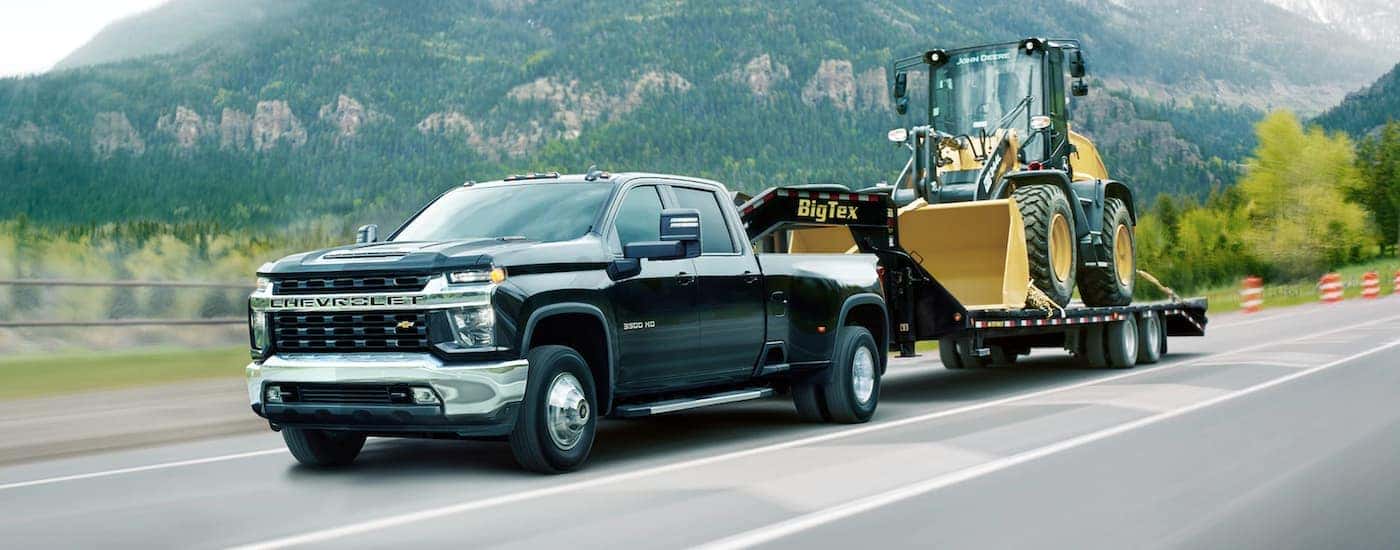 A black 2021 Chevy Silverado 3500 HD towing a front end loader.