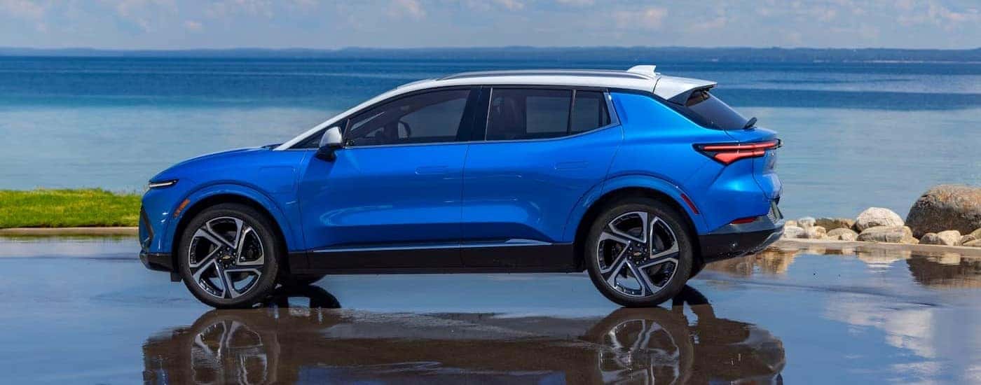 A blue 2025 Chevy Equinox EV is shown parked near an ocean.