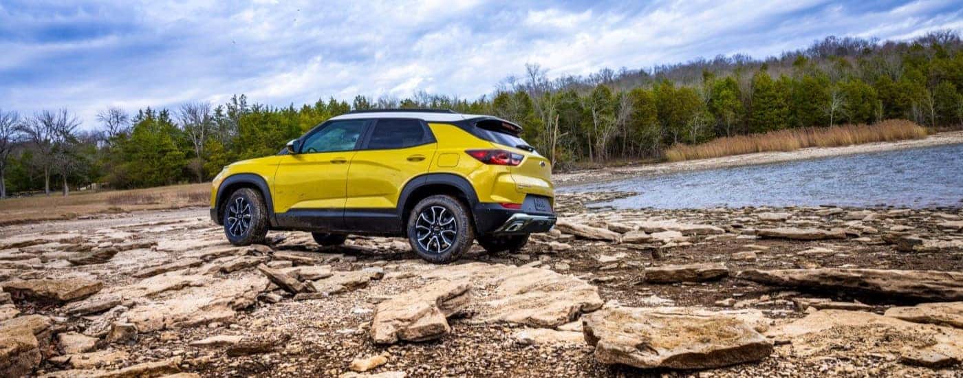 Rear left angled view of a yellow 2025 Chevy Trailblazer ACTIV parked by a lake.