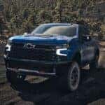 A blue 2024 Chevy Silverado 1500 ZR2 driving up a dirt hill.