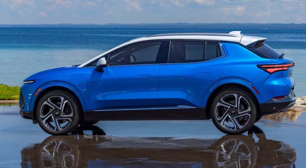 Side of a blue 2025 Chevy Equinox EV parked on wet pavement.