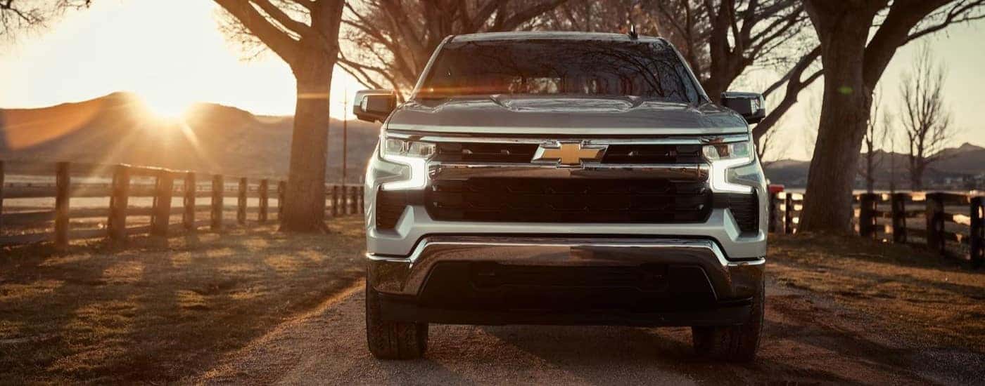 A silver 2023 Chevy Silverado 1500 for sale is shown driving by a ranch.