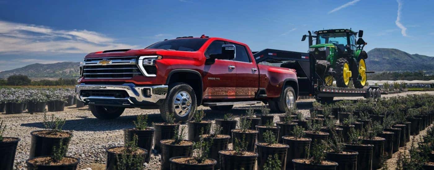 A red 2025 Chevy Silverado 3500 HD towing a tractor.
