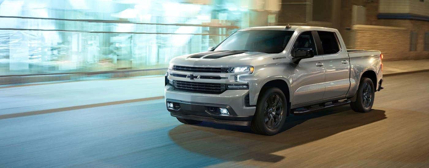A silver 2021 Chevy Silverado 1500 is shown driving on a city street at night.