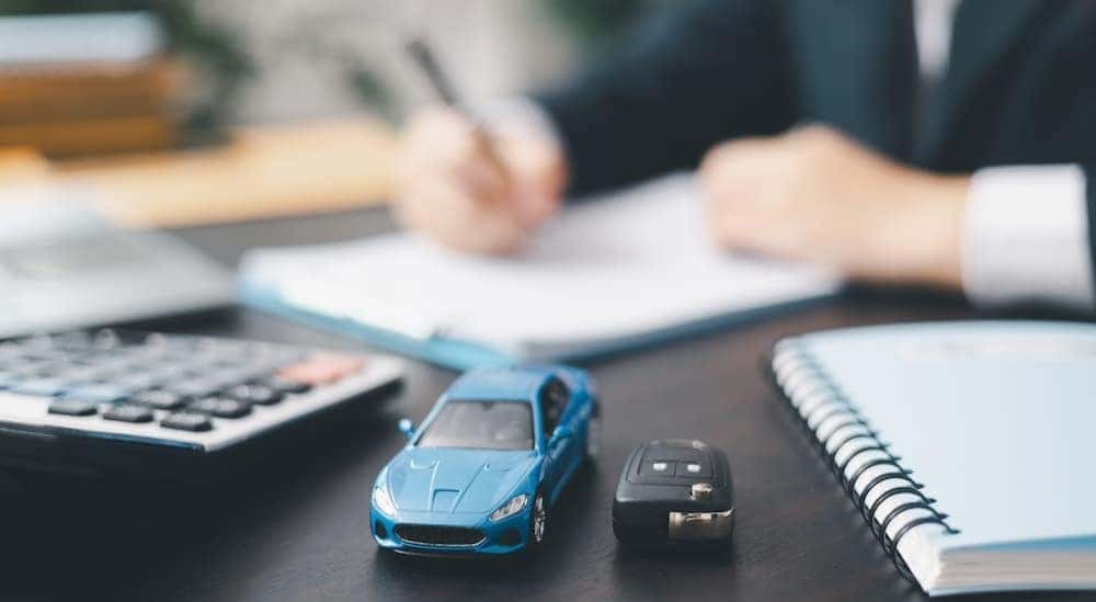 A toy car and key fob near a person signing papers.