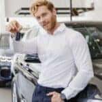A person leaning on a car holding a key fob.