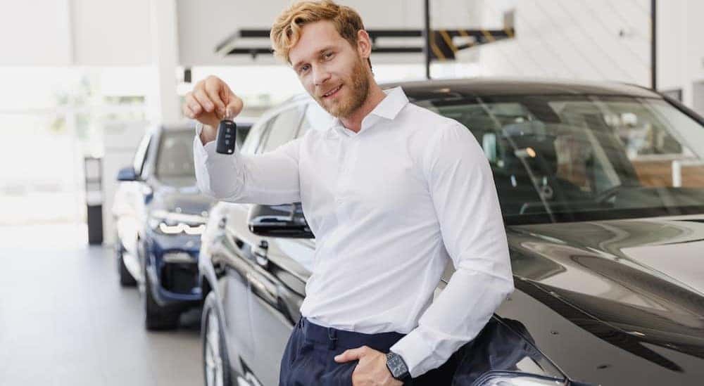 A person leaning on a car holding a key fob.