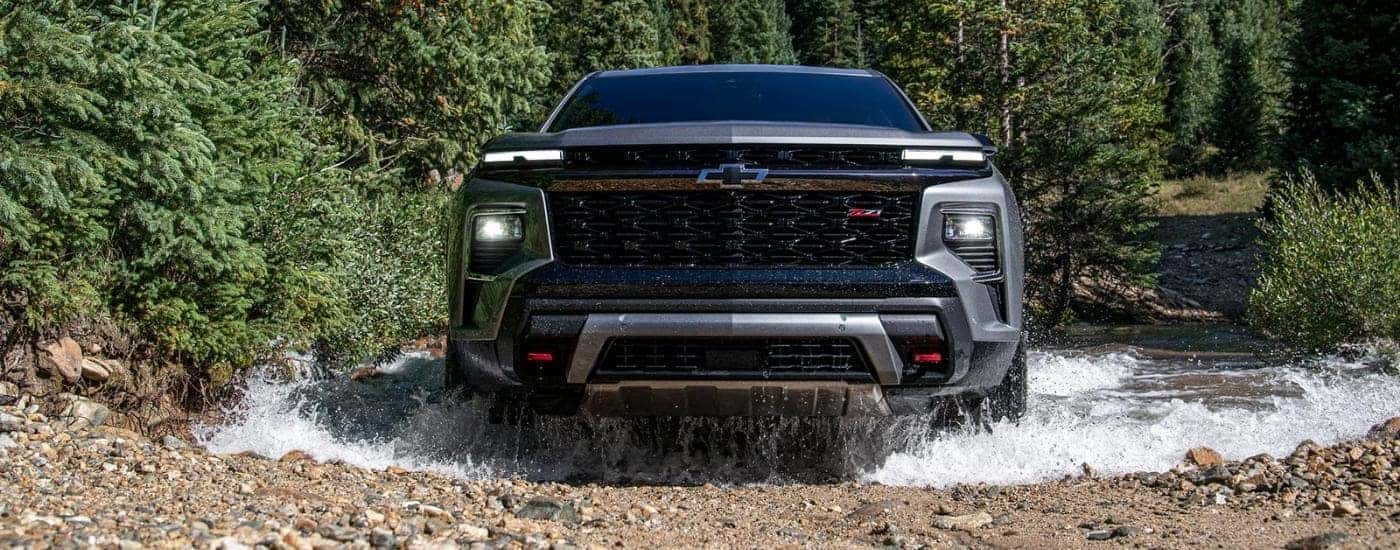 A grey 2024 Chevy Traverse for sale driving through a creek.