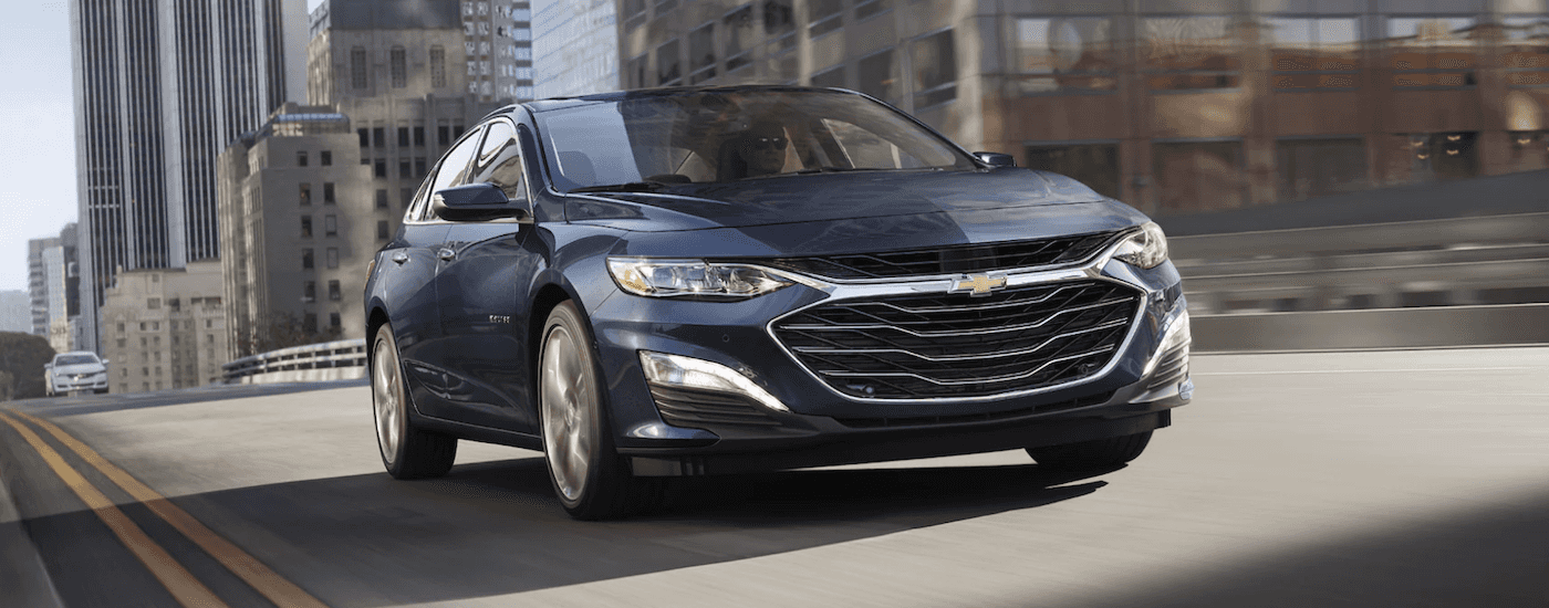 Dark blue 2022 Chevy Malibu driving through a city from a used car dealership.