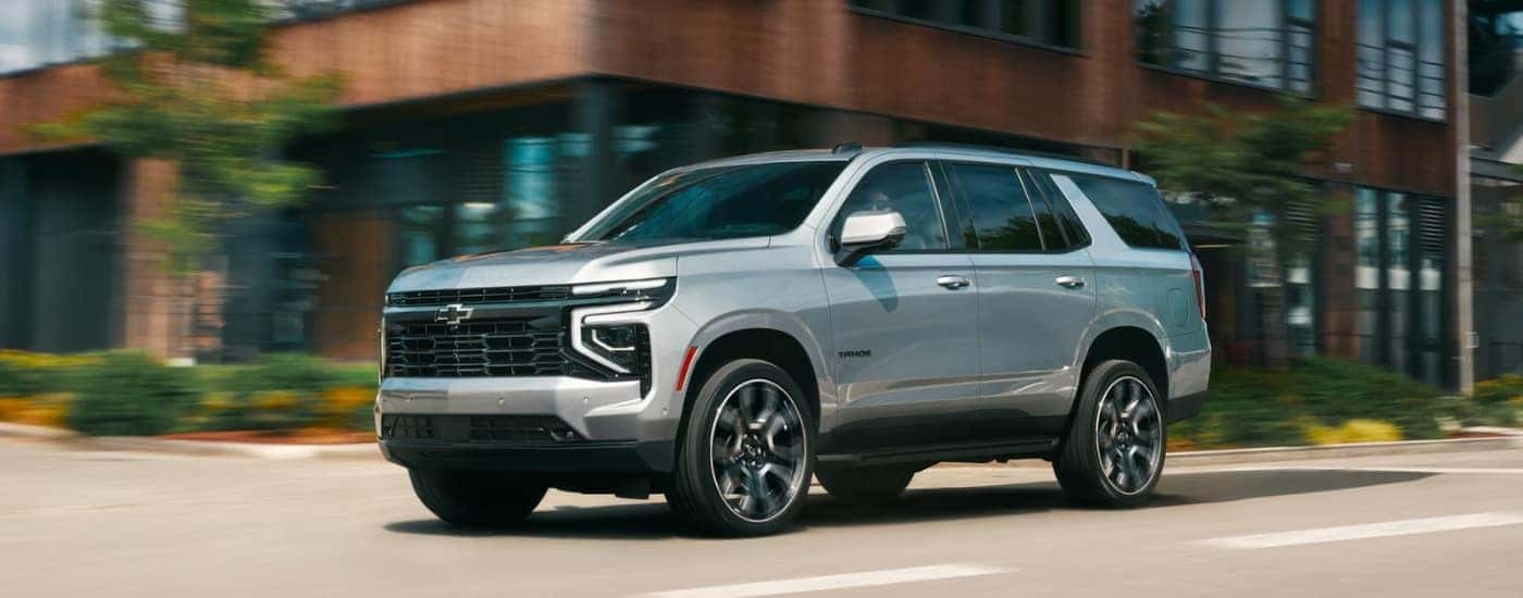 A silver 2026 Chevy Tahoe RST driving by a building.