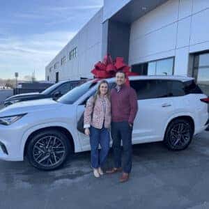 Couple standing in front of white SUV with a bow on top