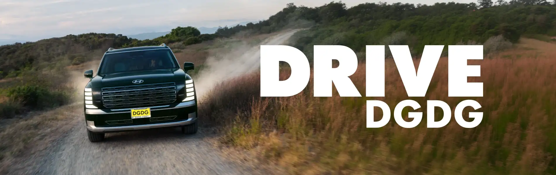 Dark green Hyundai Santa Fe SUV kicking up dust while driving along a dirt path through grassy hills.