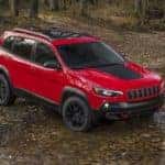 red 2021 jeep cherokee vehicle in the woods making its approach to drive through a shallow rocky river