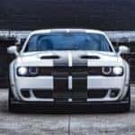 a front view of a white 2022 dodge challenger with black livery stripes parked outside a dark warehouse building
