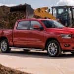 2021 red dodge ram 1500 in a construction site with soil being dumped into the truck bed by a construction vehicle