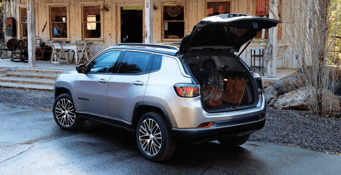 A 2024 Jeep Compass with the back hatch opened. It's parked in front of a rundown farmhouse