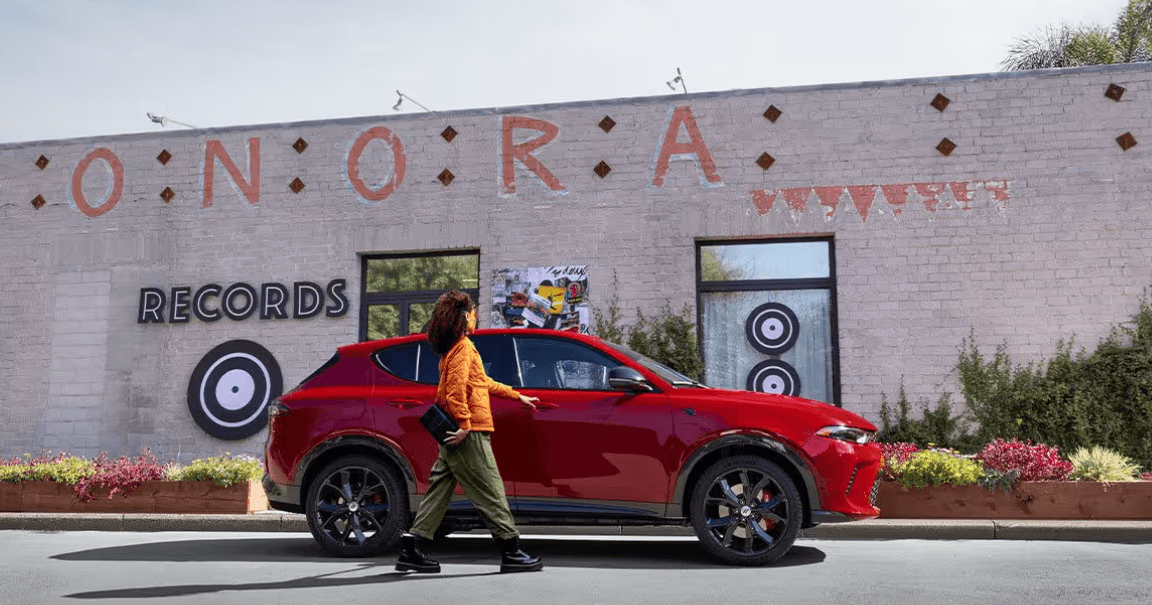 A red Dodge Hornet parked in front of a white brick building