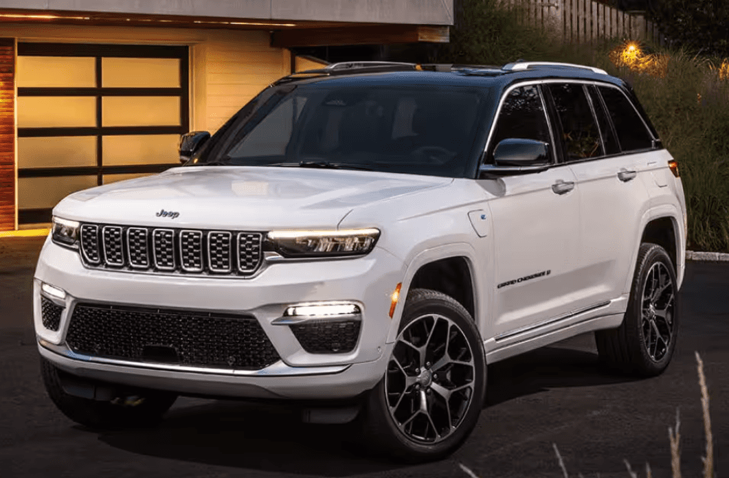 A white 2024 Jeep Grand Cherokee 4xe parked in a driveway in front of a garage