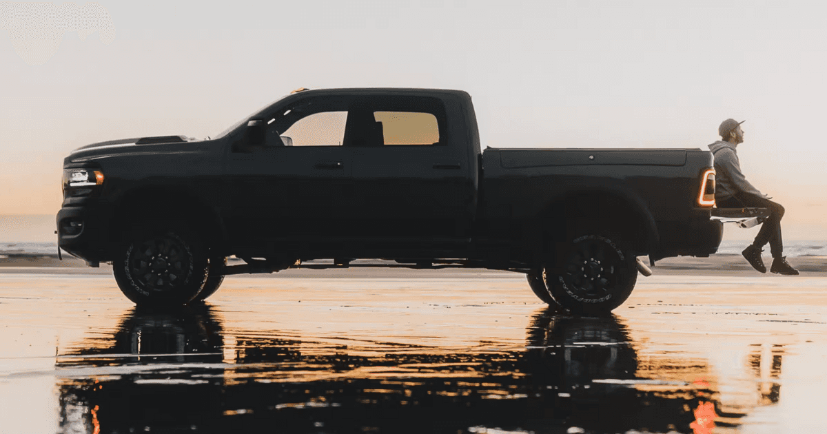 Person sitting on the bed of a ram 2500 that's parked on the shore of a beach 