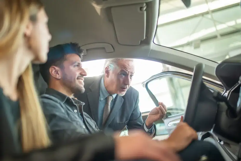 A car salesman leaning into a car where a couple is sitting.
